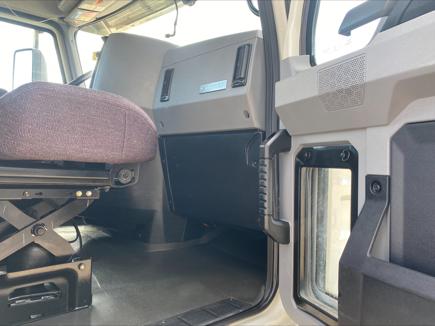 Cab interior of a 2021 Mack AN64T showing driver seat, dashboard panel, and open door