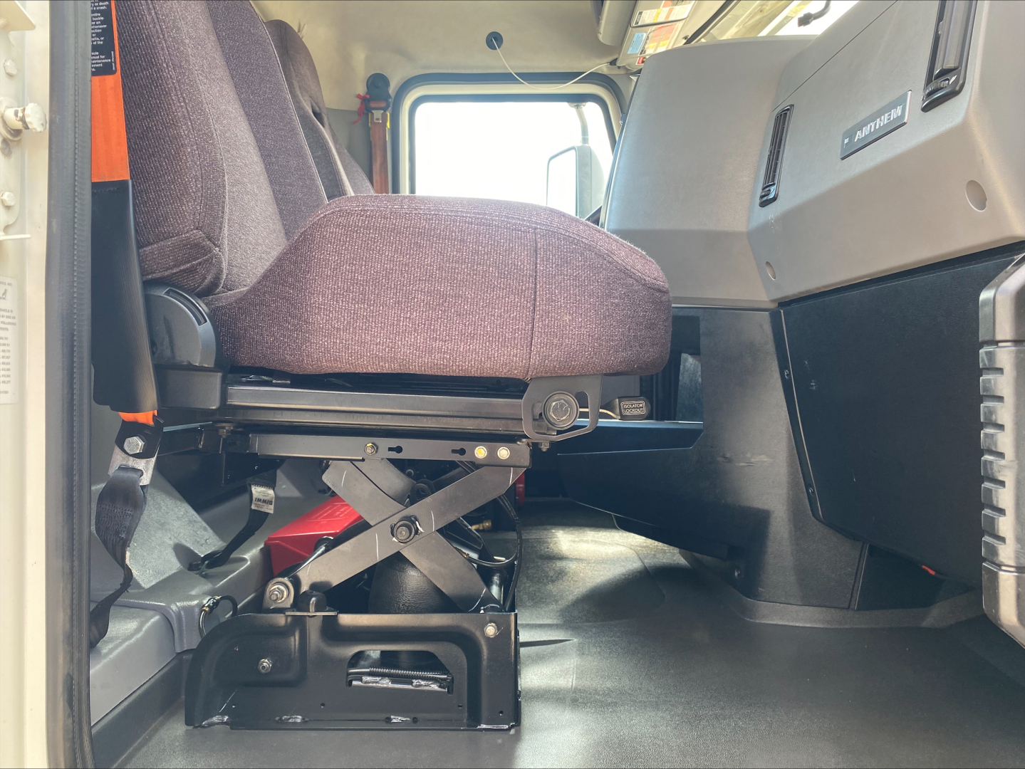Cab interior of a 2021 Mack AN64T Daycab showing driver's seat with suspension mechanism and dashboard area.