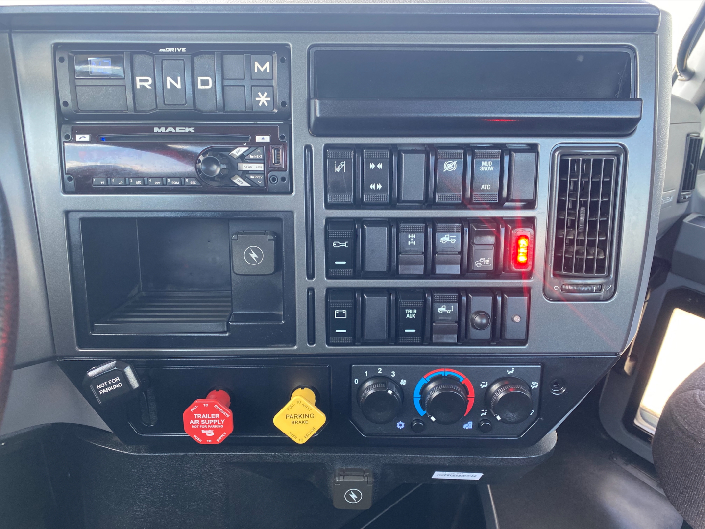 Dashboard of a 2021 Mack AN64T showing instrument cluster, stereo, controls, red and yellow hazard knobs, climate controls, and gear selector area.