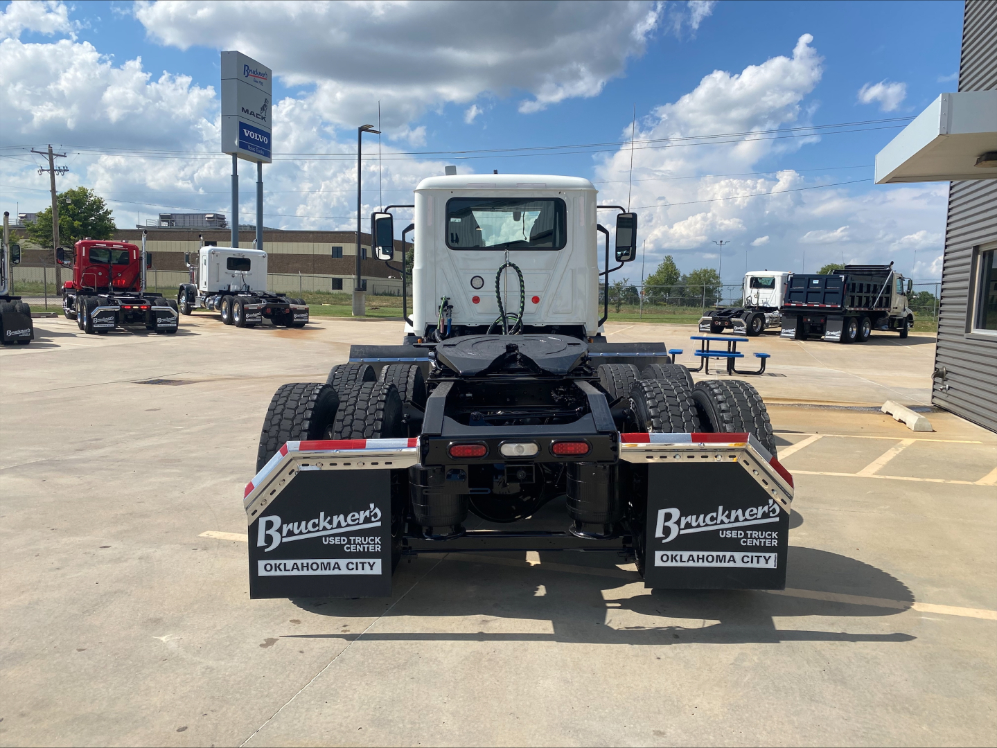 Rear view of a 2021 Mack AN64T conventional daycab truck chassis showing dual rear axles, mud flaps with Bruckner's sign and Oklahoma City markings, rear lights, and a white cab.