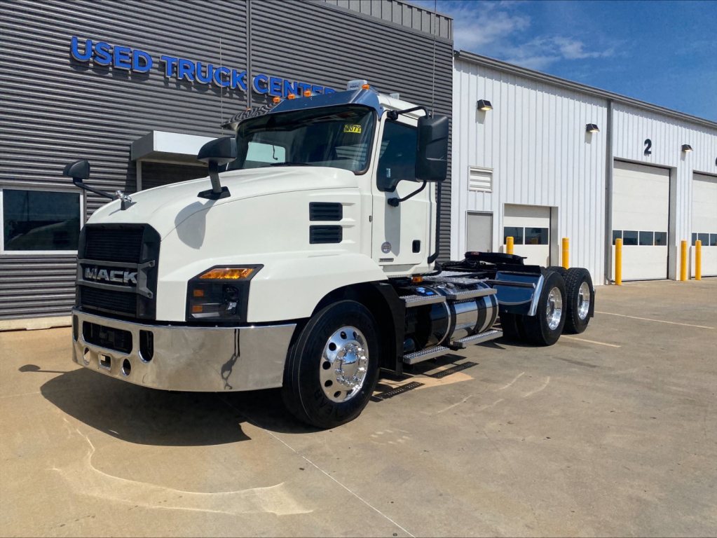 Truck: 2021 Mack AN64T conventional daycab in white, front-left view showing cab, dual rear axles, fuel tanks, and dealership building in background.