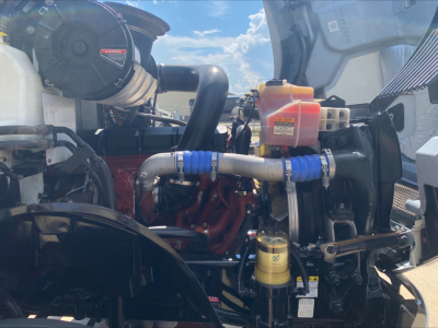 Engine compartment of a 2021 Mack AN64T daycab showing coolant reservoir, hoses, filter canister, and engine block.