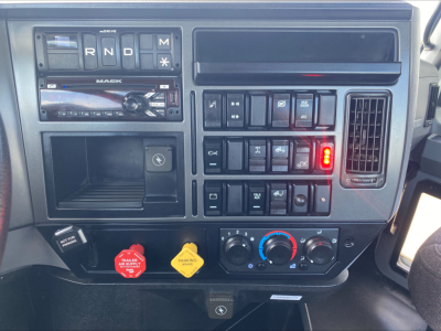 Dashboard of a 2021 Mack AN64T showing instrument cluster, stereo, controls, red and yellow hazard knobs, climate controls, and gear selector area.