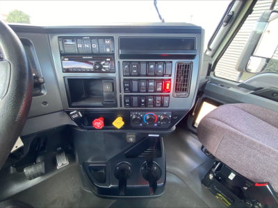 Mack AN64T truck dashboard showing gear selector R N D M, auxiliary switches, climate controls, ignition area, and steering wheel visible.