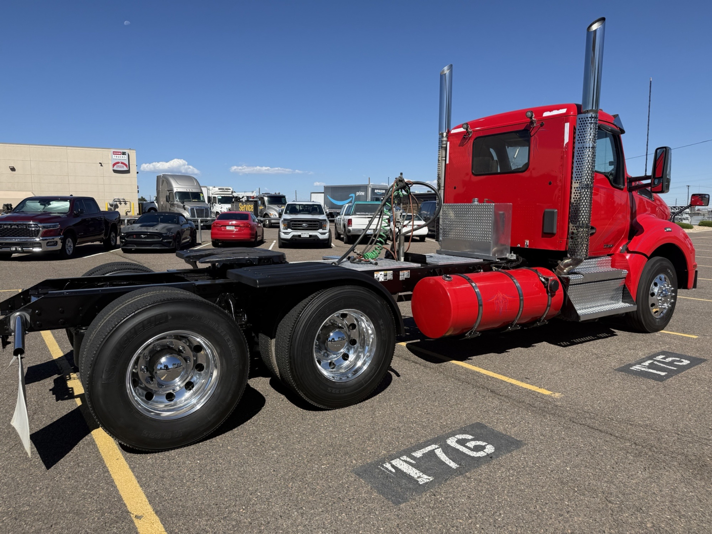 Kenworth T880 conventional daycab chassis showing red cab and dual rear axles with chrome wheels and black platform in a parking lot.