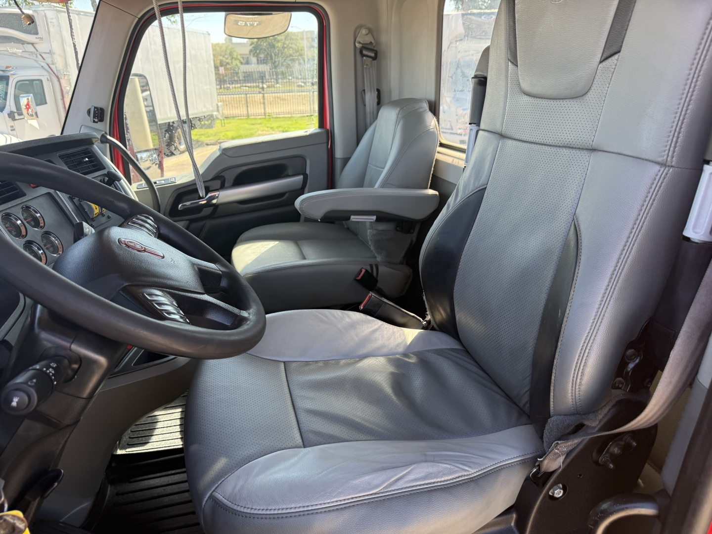 Kenworth T880 interior view showing grey leather-like seats and steering wheel, with driver and passenger seats, dashboard controls visible.