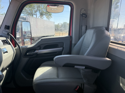 Truck cab interior showing driver seat and armrest from Kenworth T880 cab; front door panel and dashboard visible; light gray seats, window with exterior trailers.