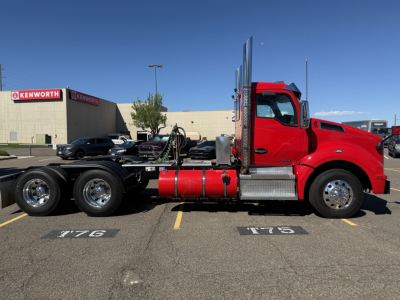 Kenworth T880 daycab truck side profile showing red cab, chrome exhaust stacks, and fuel tanks in parking lot.