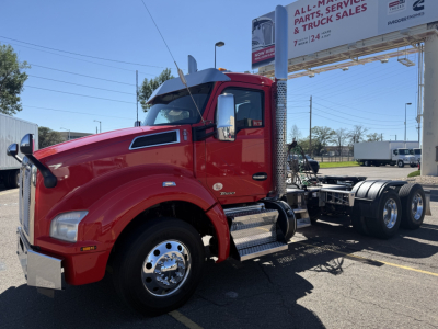 Kenworth T880 cab shows red exterior, side mirror, hood with vents, chrome wheel, and chassis exposed. Billboard in background with text partially legible.