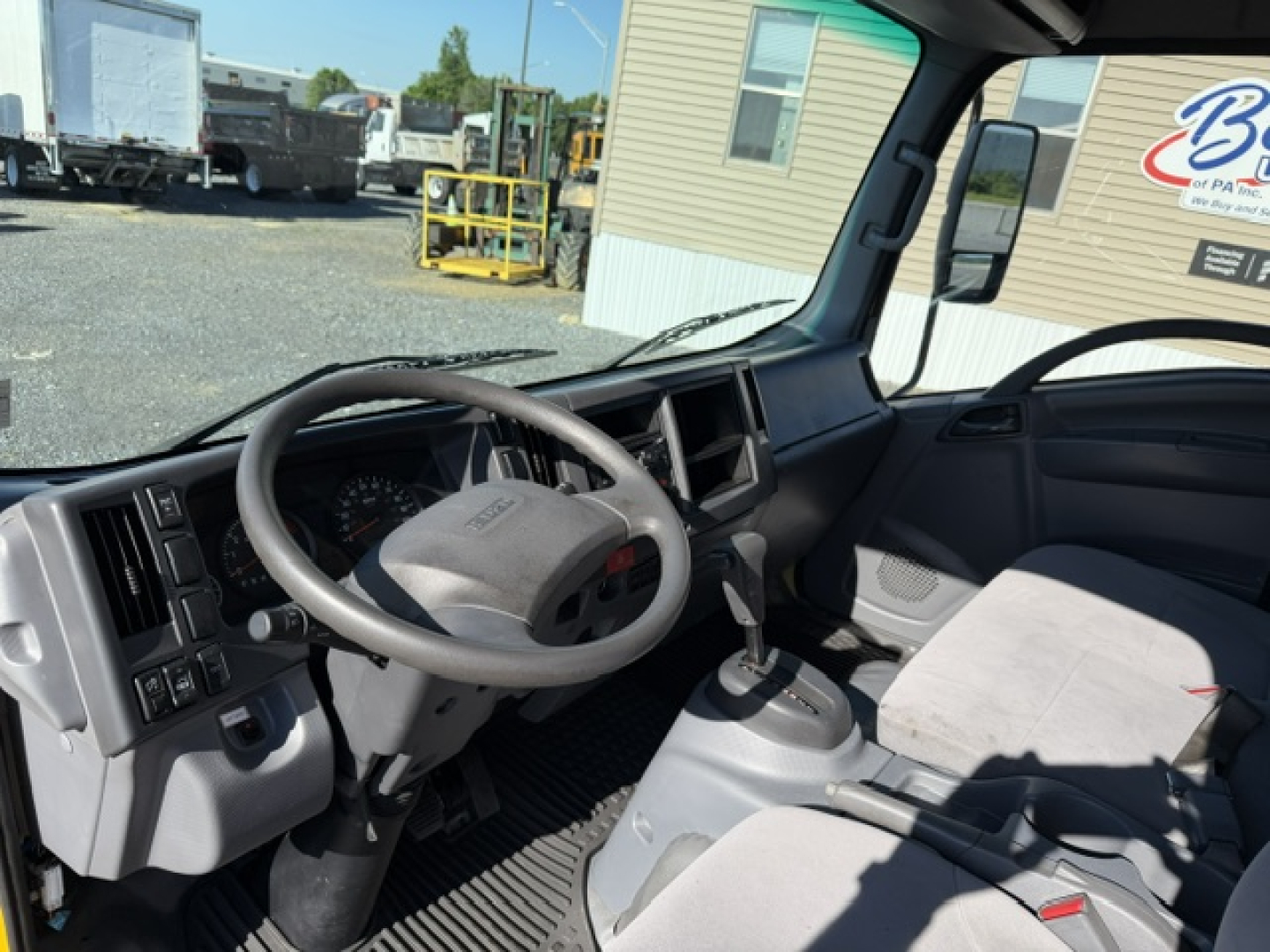 Isuzu NPR truck interior showing steering wheel, dashboard, and gear selector with light gray seats.