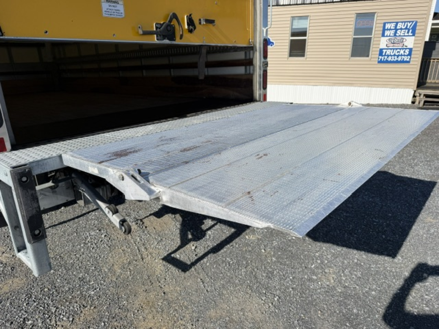 Isuzu NPR truck rear loading ramp extended showing platform and hitch with metalwork and wheel well in cargo area.