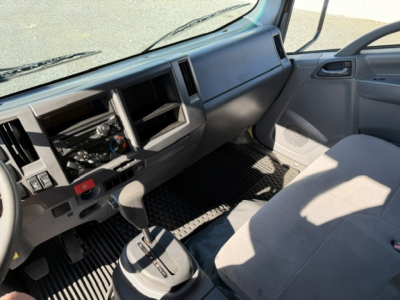Isuzu NPR cab interior showing dashboard with exposed stereo, air vents, gear selector, and steering wheel from the driver's seat perspective.
