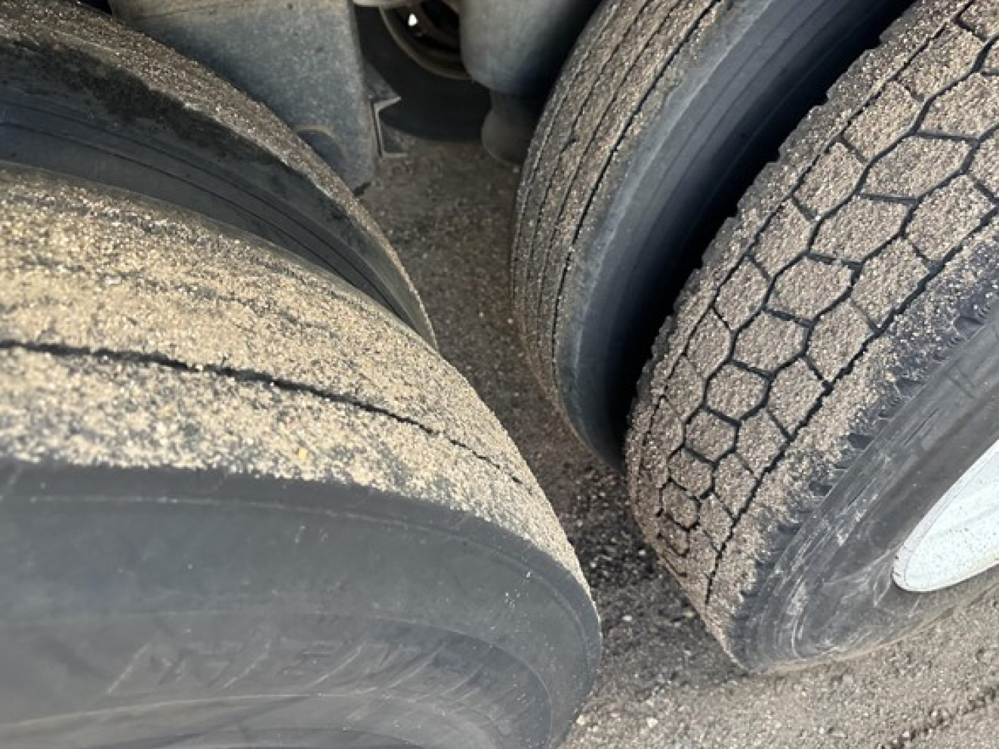 Trailer wheel area of a 2015 Timpte Super Hopper showing two tires with tread and dust; part of the trailer’s landing gear not visible; close-up of tire treads.
