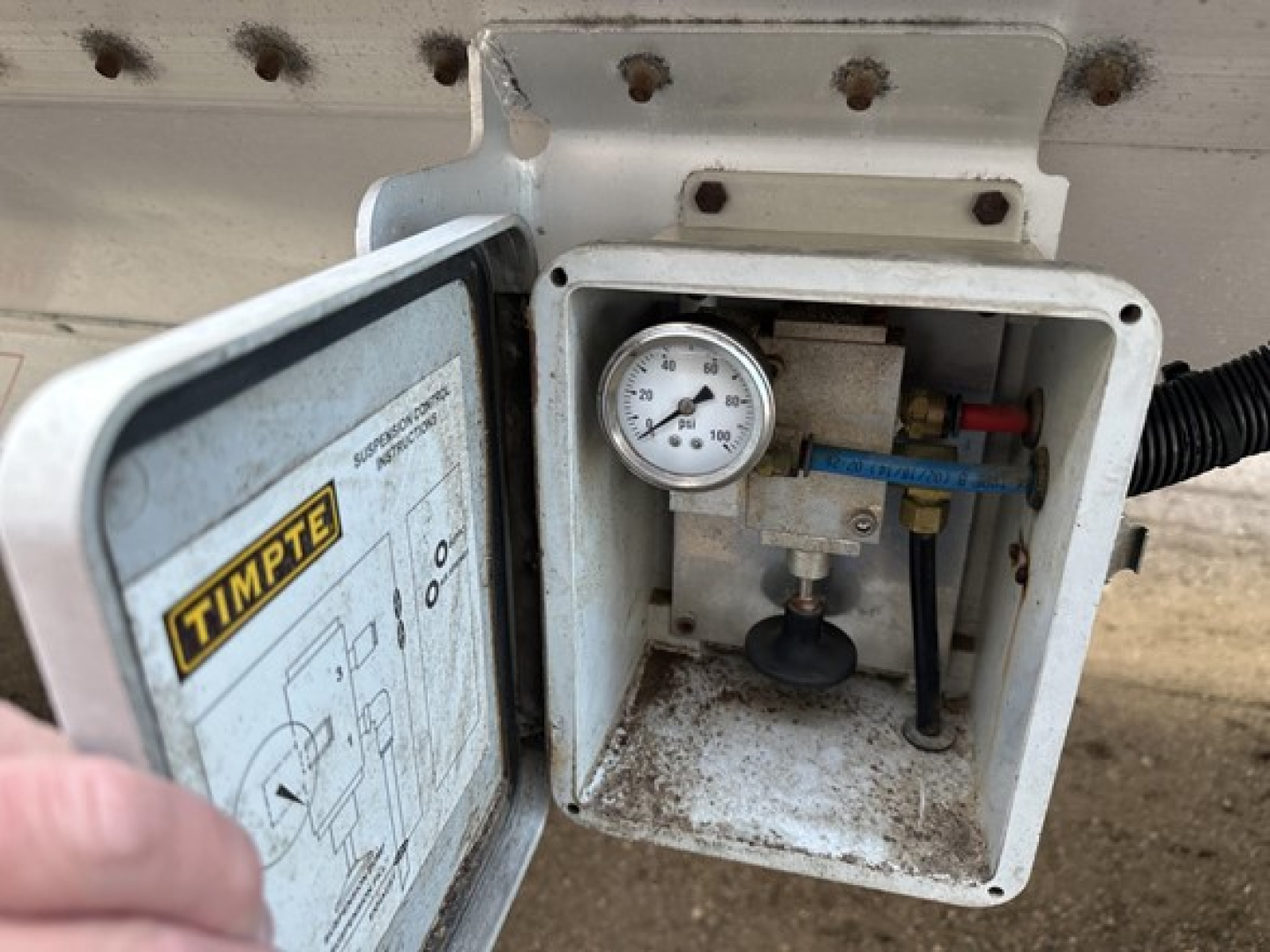 Timpte Super Hopper trailer service box showing pressure gauge and valve with blue handle and wiring inside a weathered white enclosure.