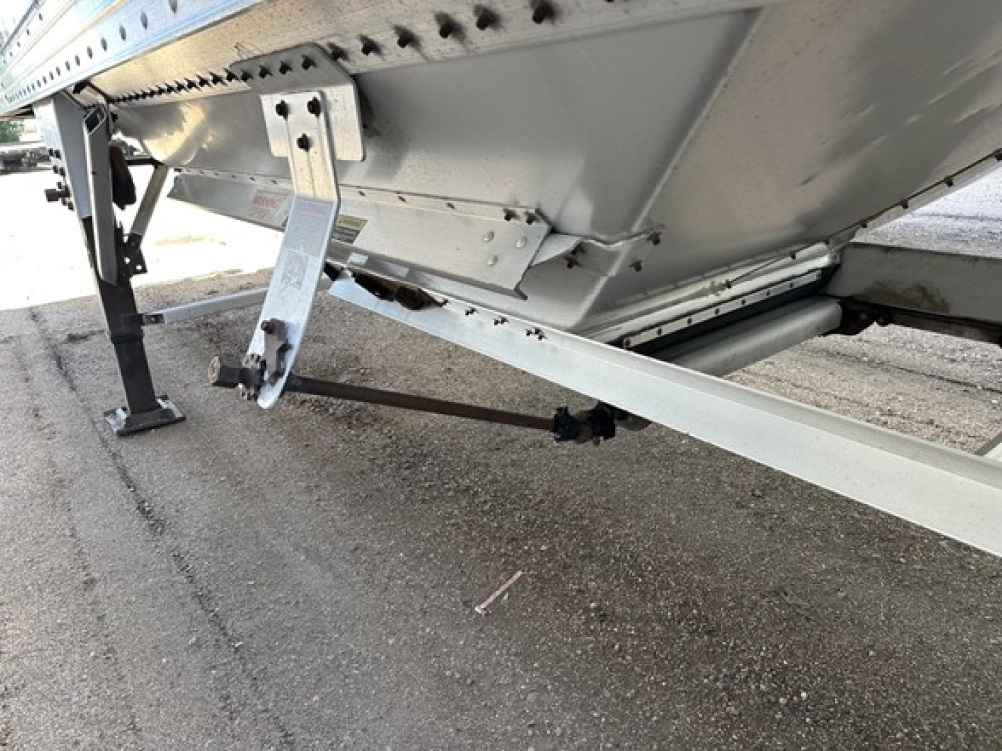 Trailer underside showing support leg, hitch arm, and frame of a Timpte hopper trailer with riveted side panels and ladder bracket.