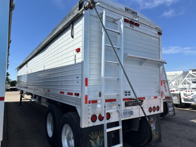 Tall white Timpte Super Hopper trailer in profile view showing side panels, rear ramp, and ladder with black branding, dual rear tires, and reflective strips.