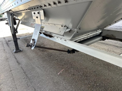 Trailer underside showing support leg, hitch arm, and frame of a Timpte hopper trailer with riveted side panels and ladder bracket.