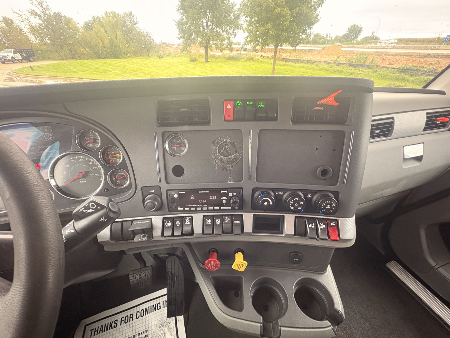 Truck cab interior dashboard of a 2022 Kenworth T680 showing steering wheel, gauges, center console with controls and vents, two cup holders, and assorted knobs.
