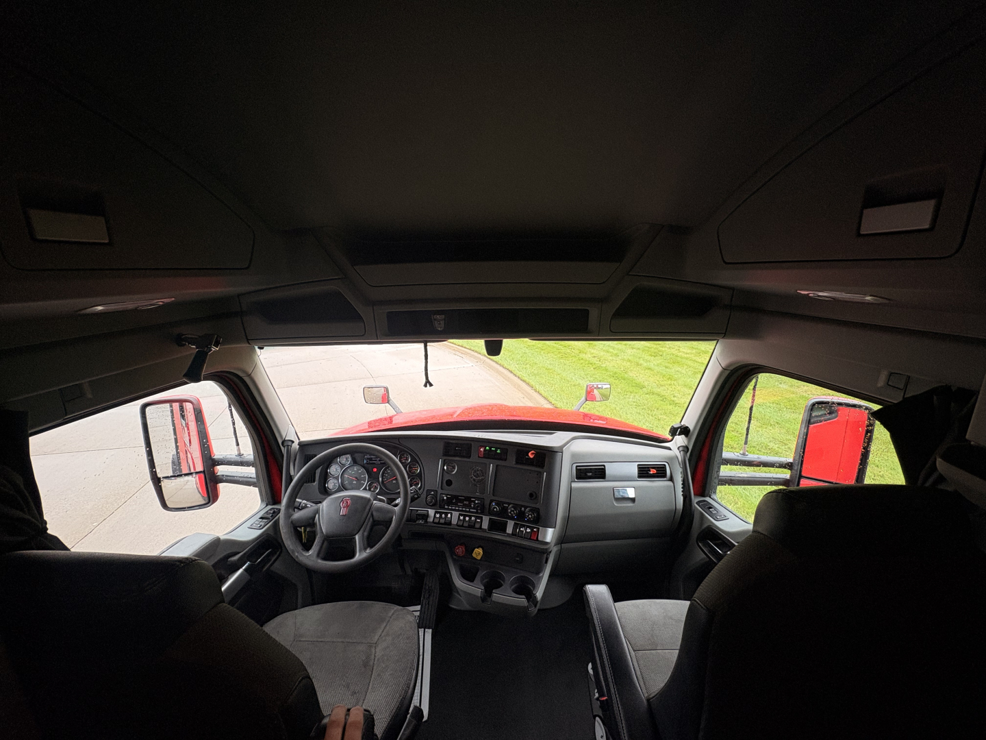 Cab interior of a 2022 Kenworth T680 truck showing steering wheel, dashboard, and driver seat from front passenger perspective.