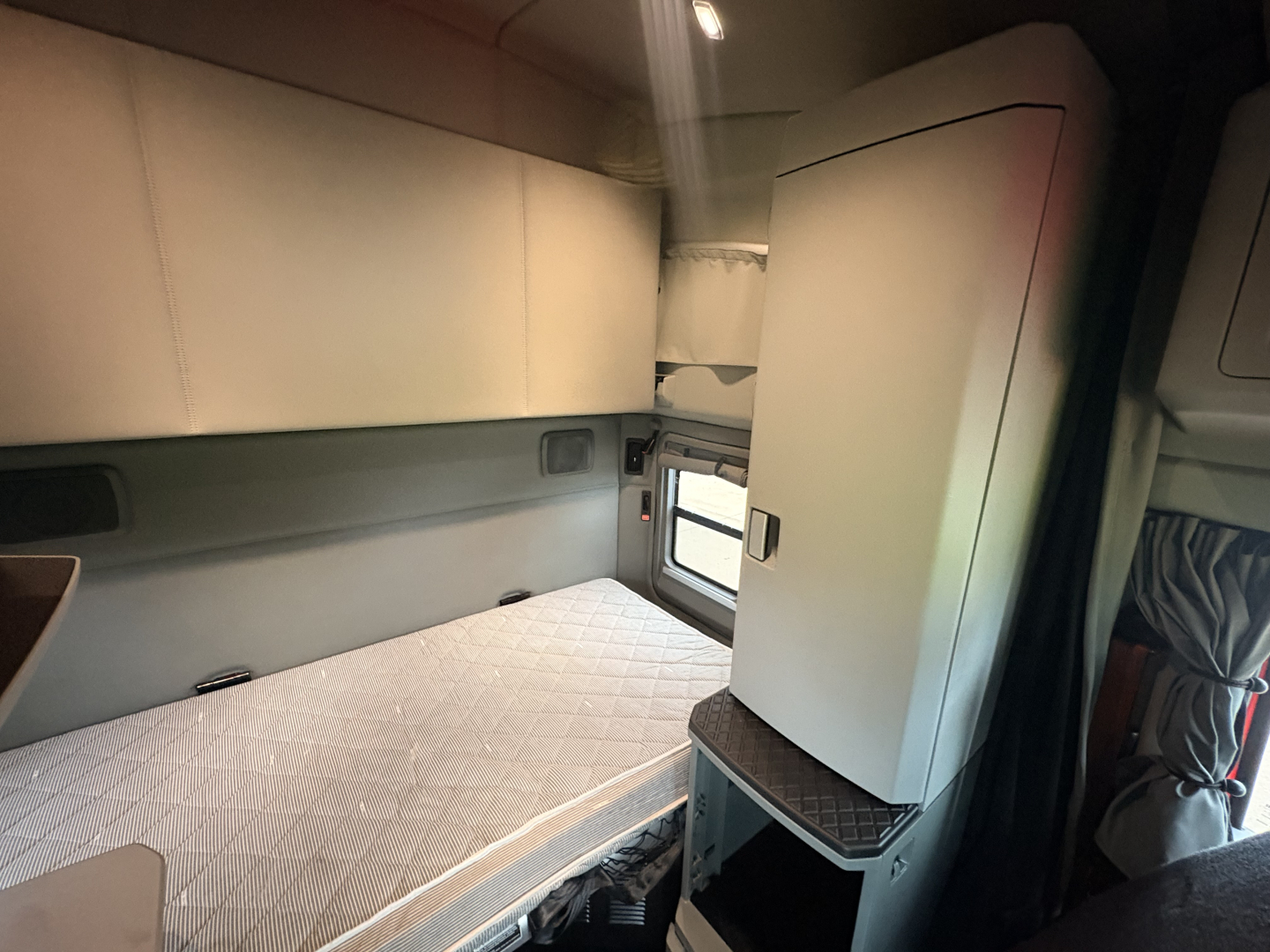 Interior sleeper cab of a 2022 Kenworth T680 showing bed area and storage cabinet.