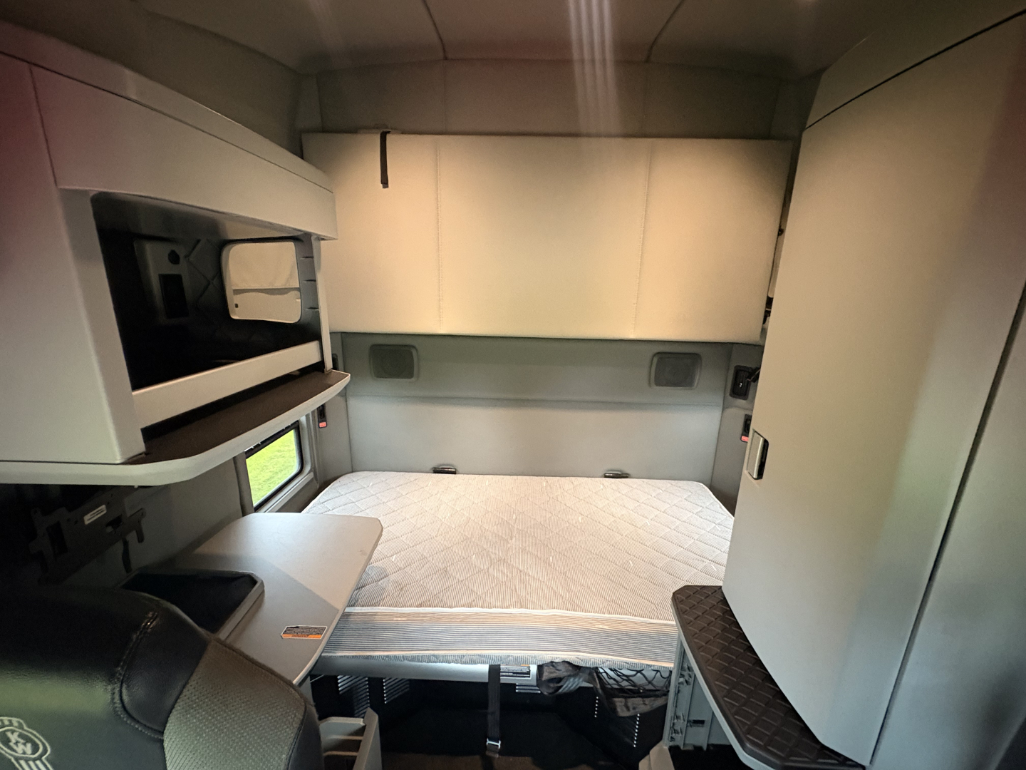Kenworth T680 sleeper cab interior showing storage compartments and bunk area with quilted mattress, side shelves, and cabin walls.