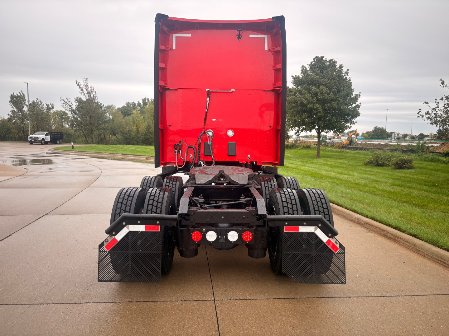 Kenworth T680 rear view showing chassis, dual rear axles, mudflaps, and red sleeper cab in a parking area.