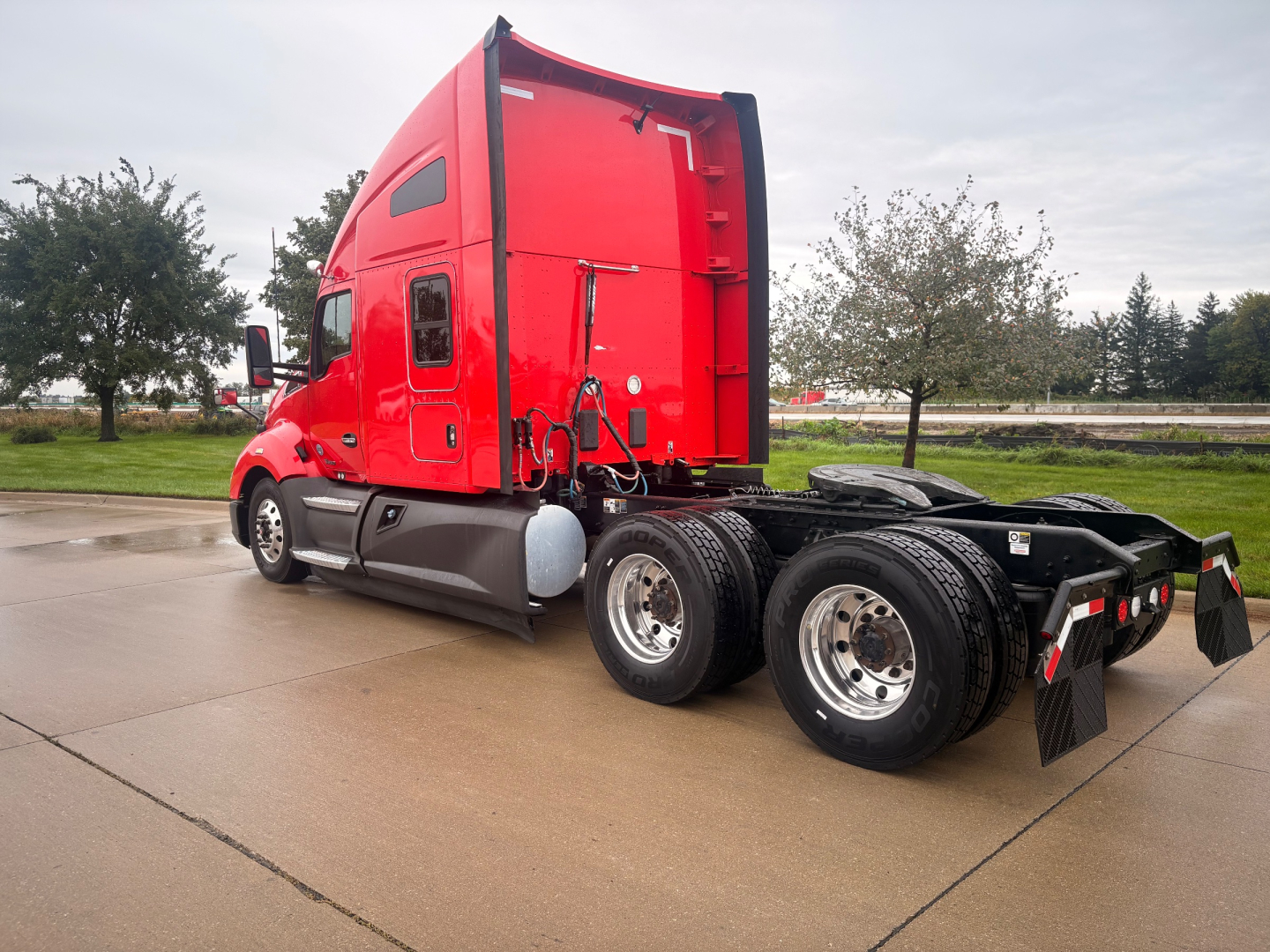 Kenworth T680 sleeper cab truck side view showing red cab and dual rear axles with black mud flaps and chrome wheels.