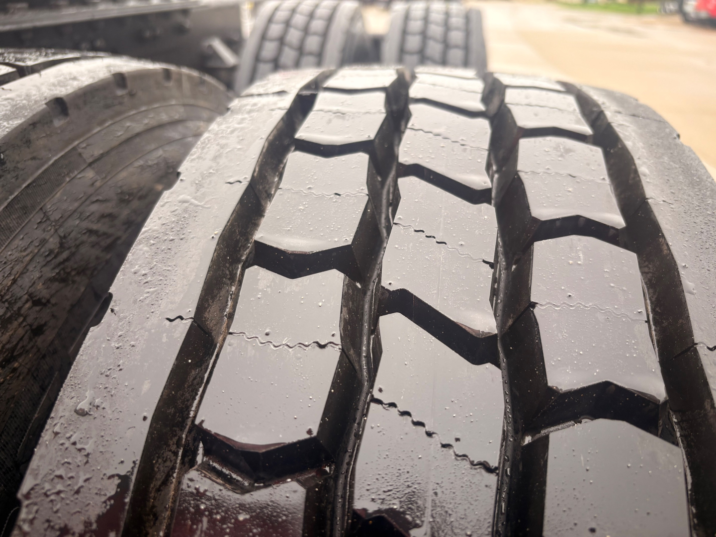 Truck wheel tread close-up showing large, directional tread blocks and wet rubber on a Kenworth T680 axle.