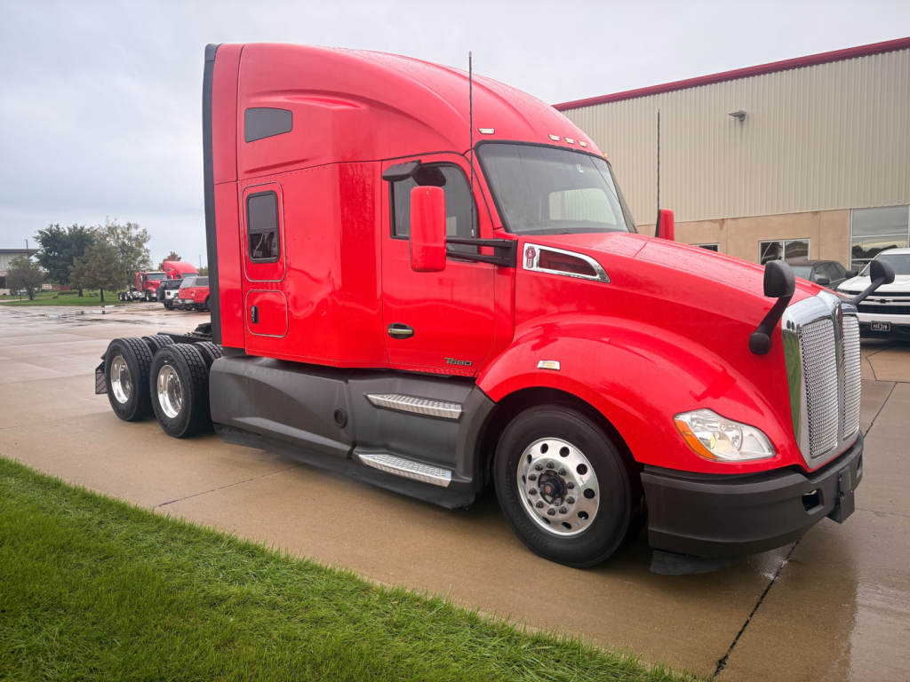 Kenworth T680 red sleeper cab tractor from side/front angle with three rear axles and chrome wheels.