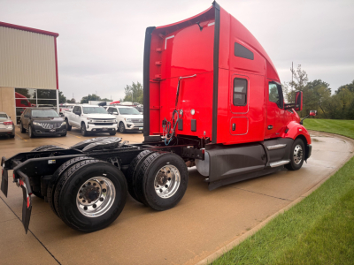 Kenworth T680 conventional sleeper truck side view showing red cab and rear dual rear axles with mudflaps and wheel rims.