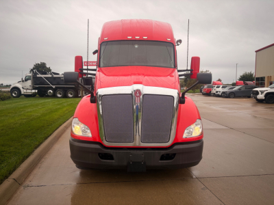 Front view of a red 2022 Kenworth T680 truck in a dealership lot. Bold chrome grille with Kenworth emblem, large black bumper, headlights on both sides.