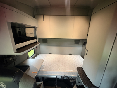 Kenworth T680 sleeper cab interior showing storage compartments and bunk area with quilted mattress, side shelves, and cabin walls.