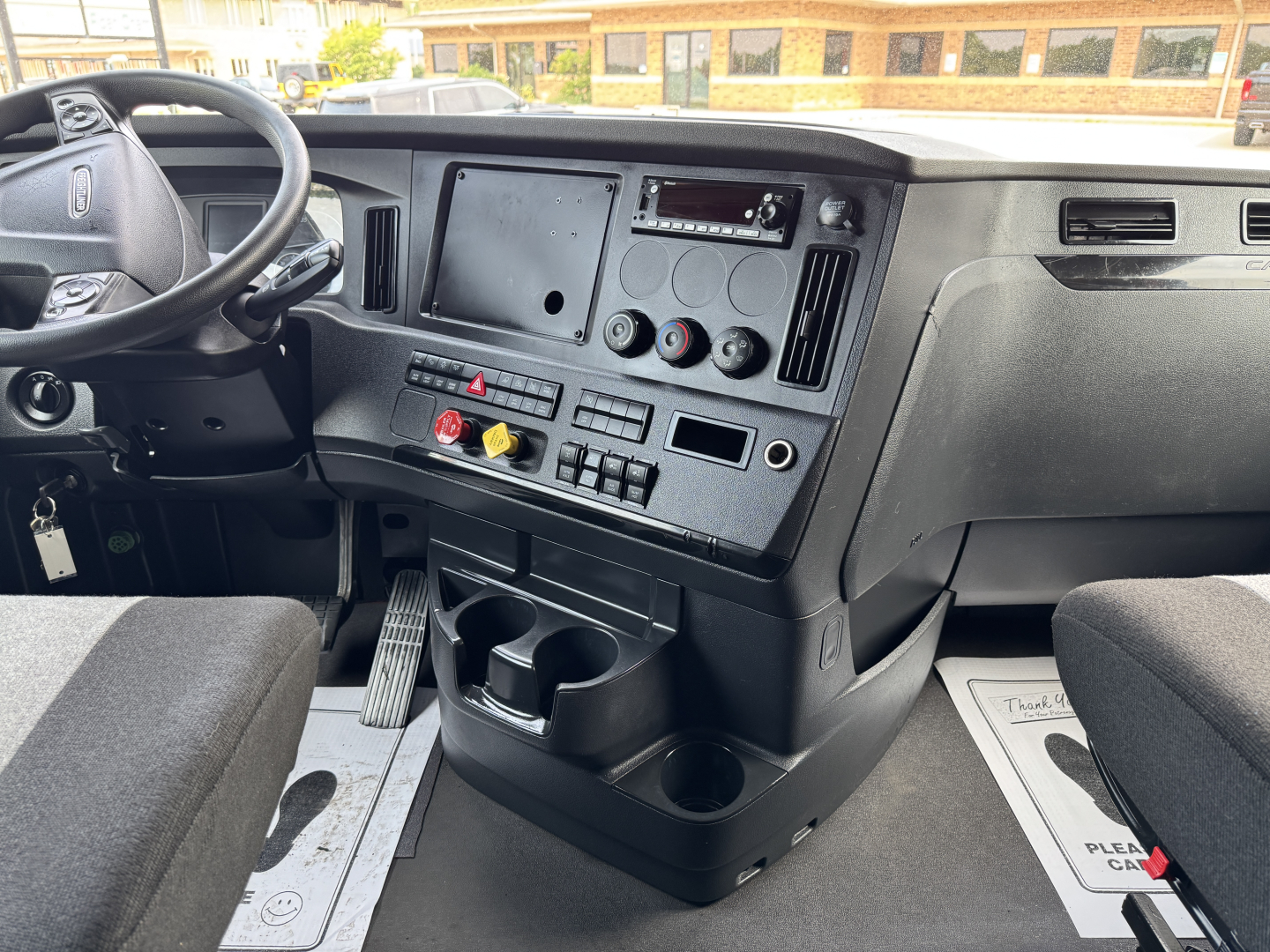 Cab interior of a Freightliner Cascadia 126 truck showing steering wheel, dashboard with controls, cup holders, and pedal area.