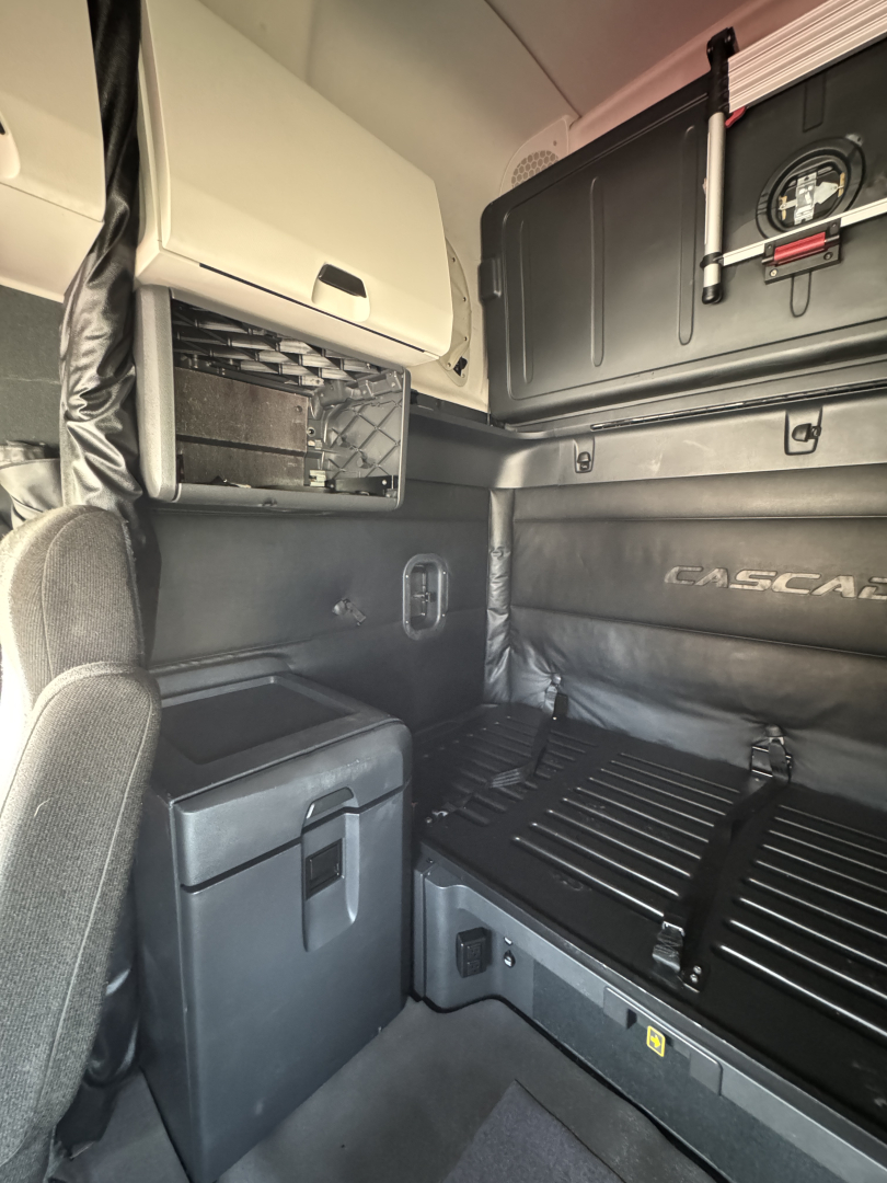 Freightliner Cascadia 126 sleeper cab interior showing sidewall storage, overhead compartments, and bed area with Ascend branding on panel.