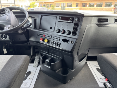 Cab interior of a Freightliner Cascadia 126 truck showing steering wheel, dashboard with controls, cup holders, and pedal area.