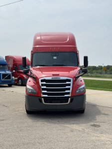 Front view of a red 2023 Freightliner Cascadia 126 semi-truck with grille, chrome bars, black side mirrors, and gray bumper.