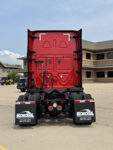 Rear view of a red Freightliner Cascadia 126 semi truck tractor chassis in a parking lot, with Kordell mud flaps and rear lights.