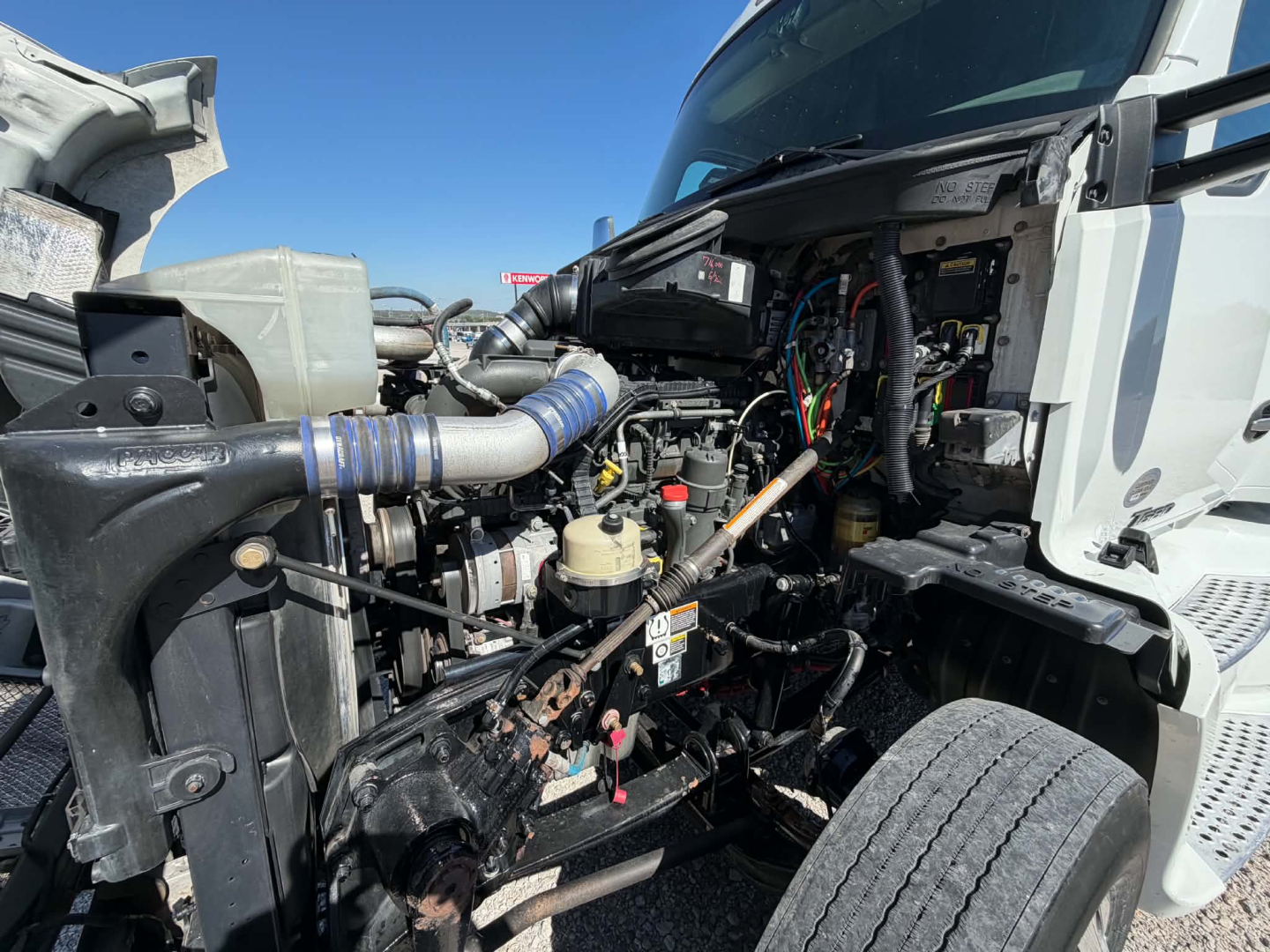 Kenworth T680 engine bay view showing fuel lines, hoses, wiring harness, and various components under the hood.