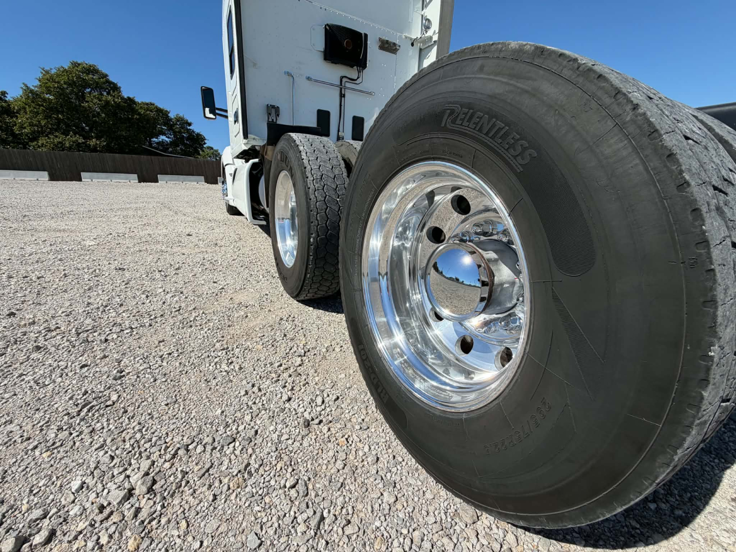 Kenworth T680 truck front wheels and front portion with polished steel rims and tire tread visible in a gravel lot.