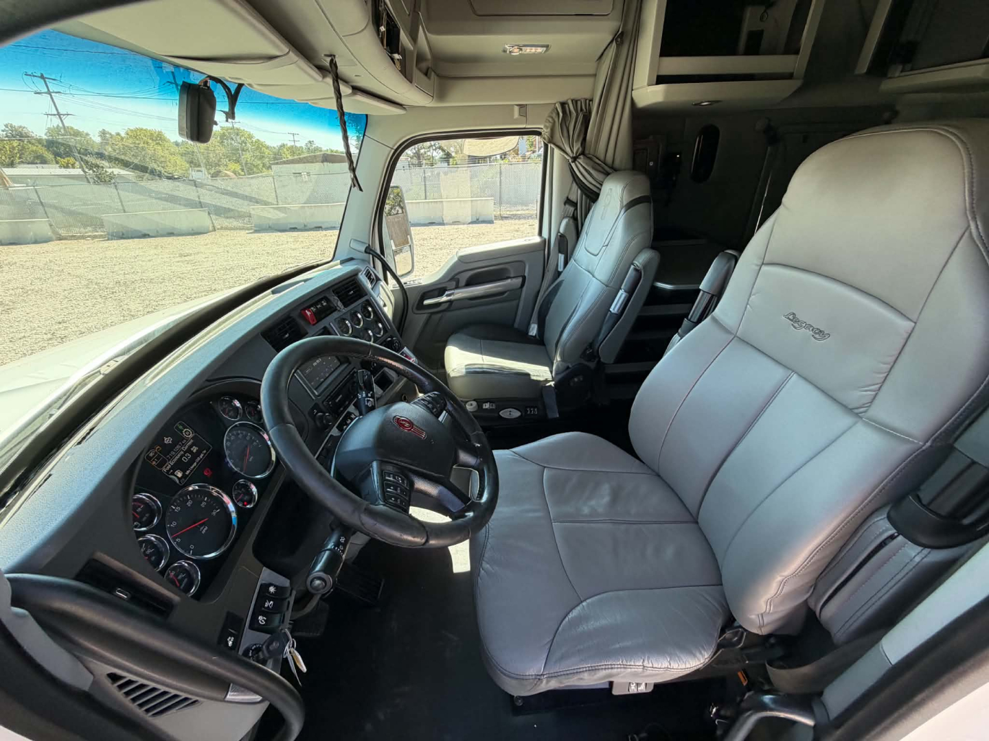 Truck cab interior of a 2019 Kenworth T680 showing steering wheel, dashboard, driver seat, and passenger seat with light gray upholstery.