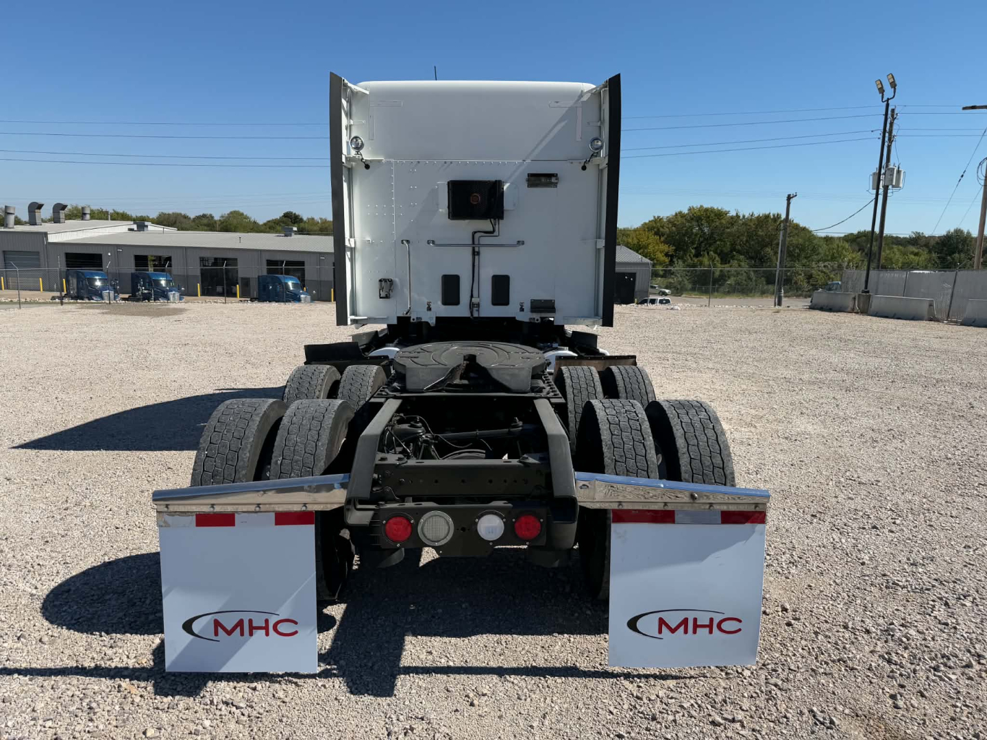 Rear view of a Kenworth tractor with fifth wheel, dual rear axles, and MHC mud flaps showing MHC logos.