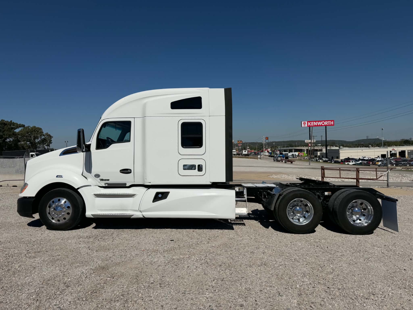 Kenworth T680 tractor unit side view showing sleeper cab and dual rear axles in a gravel lot.