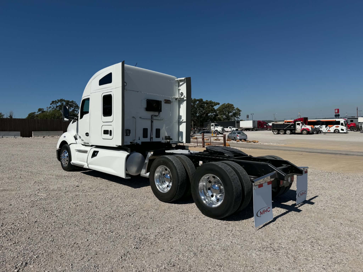 Side view of a white 2019 Kenworth T680 tractor with sleeper cab, showing rear dual axle, fifth wheel area, and sign on mudflap.