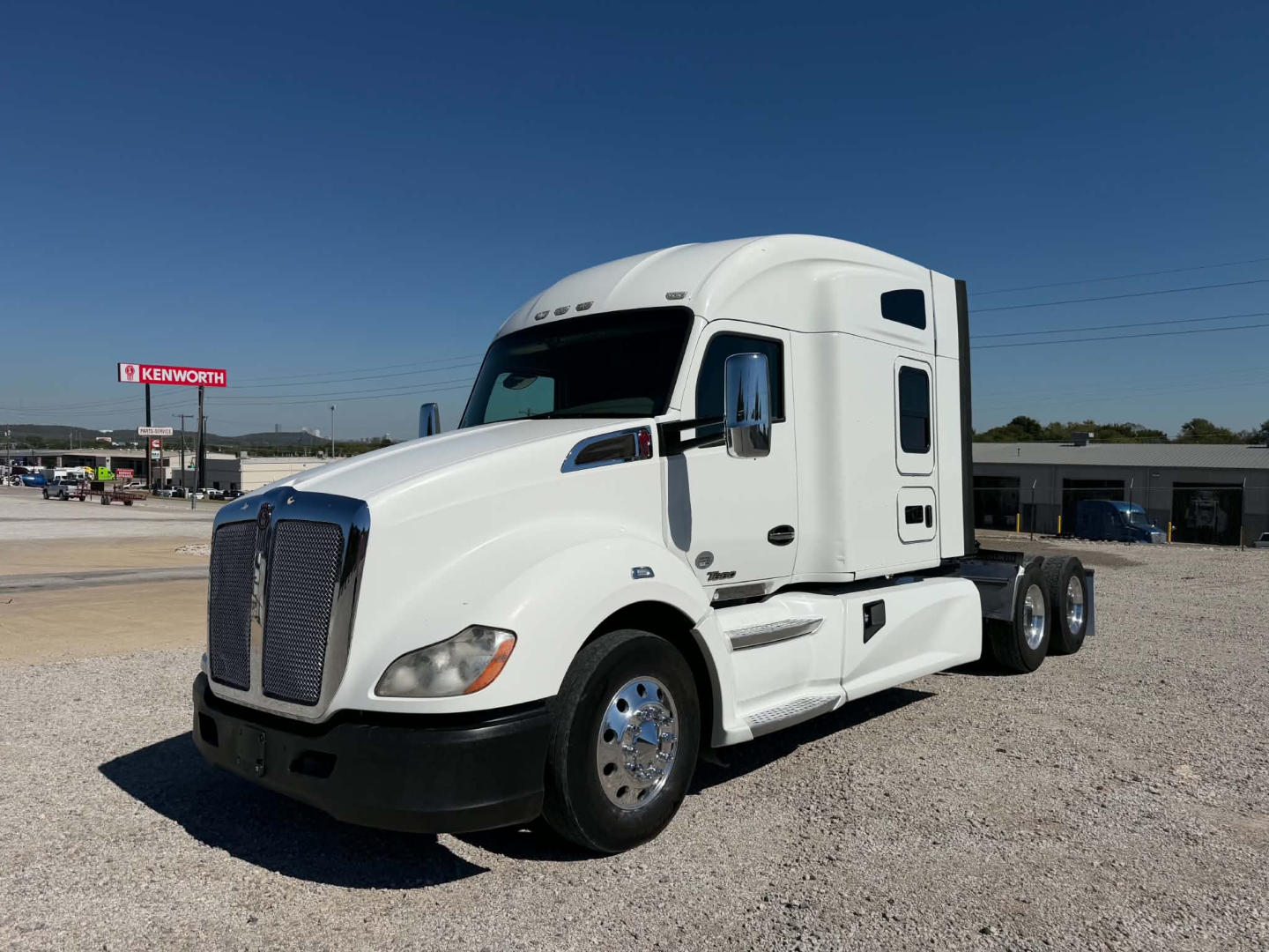 Kenworth T680 semi-truck in a dealership lot, white exterior with sleeper cab and chrome wheels.