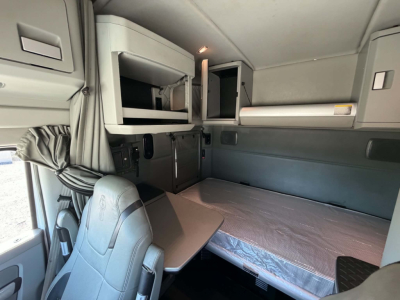 Interior cab view of a 2019 Kenworth T680 sleeper: bunk bed, overhead cabinets, window curtains, and workspace table visible.