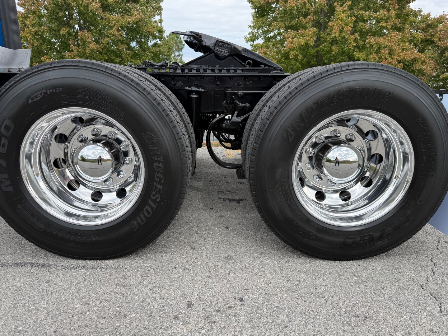 Kenworth truck axle with two Bridgestone tires and polished chrome wheels, chassis frame visible between wheels.