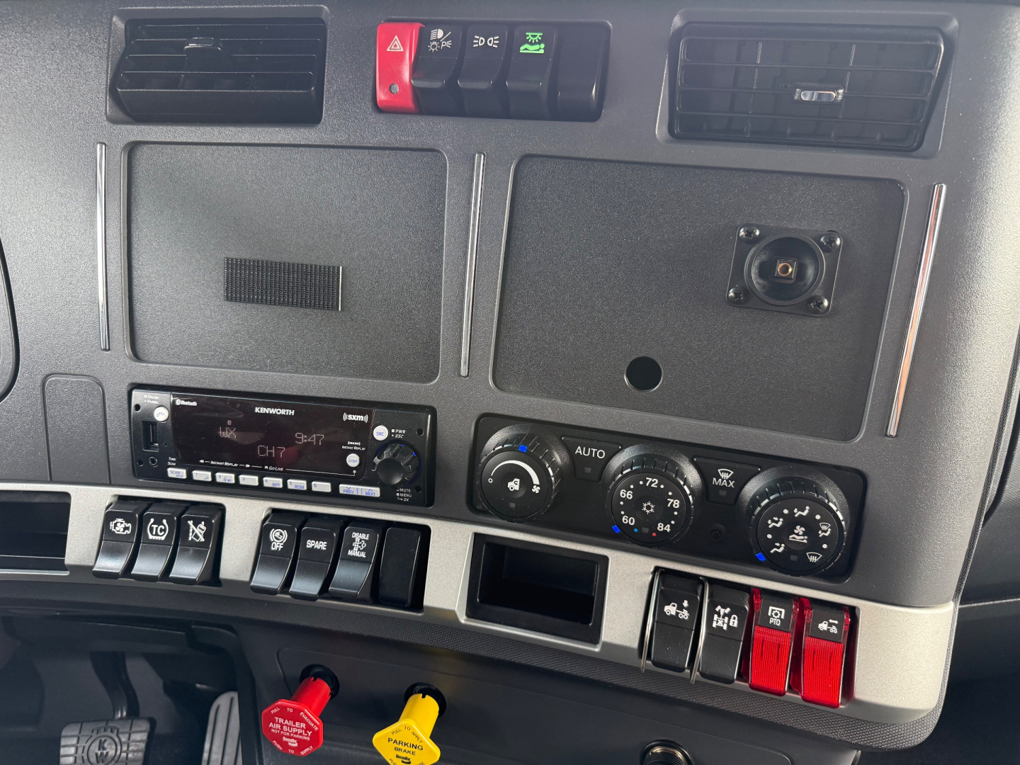 Dashboard panel of a 2023 Kenworth T680 showing switches, vents, climate controls, and a radio unit.
