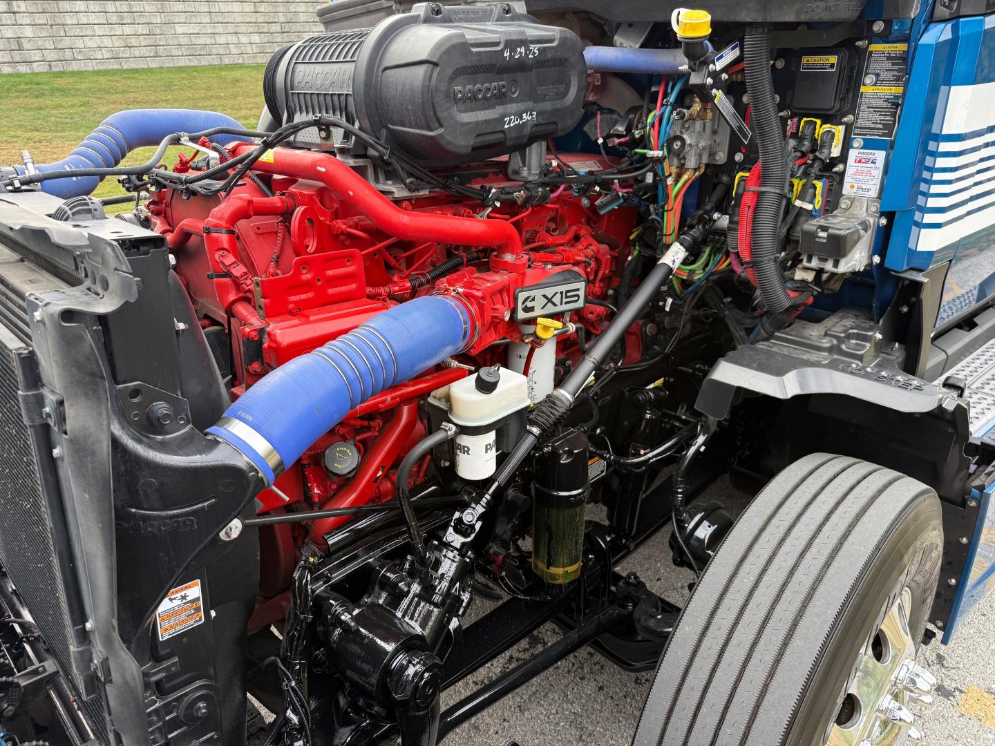 Kenworth T680 engine bay showing red engine with blue intercooler hose, multiple hoses and components in view.