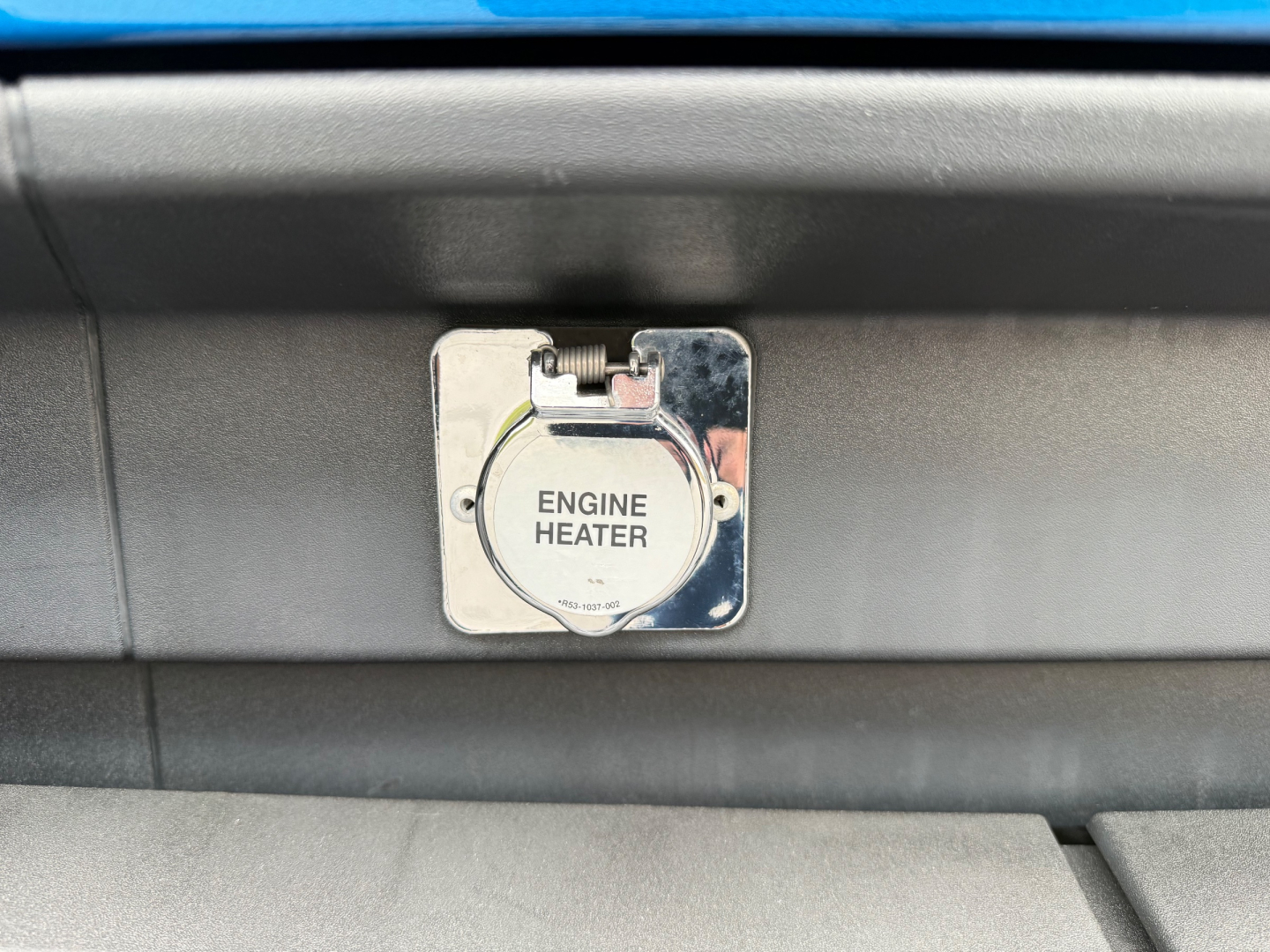 Kenworth truck engine bay area showing a metal engine heater access panel with circular cap labeled ENGINE HEATER.
