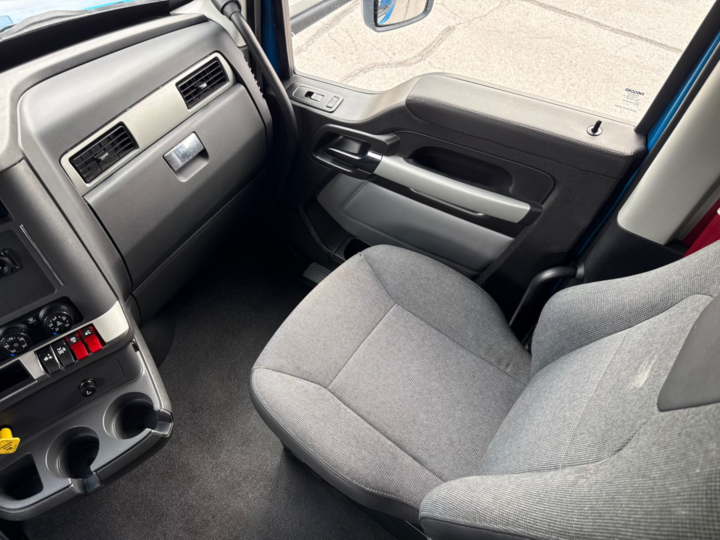 Cab interior of a 2023 Kenworth T680 semi-truck showing driver seat, dashboard, and center console with cup holders.